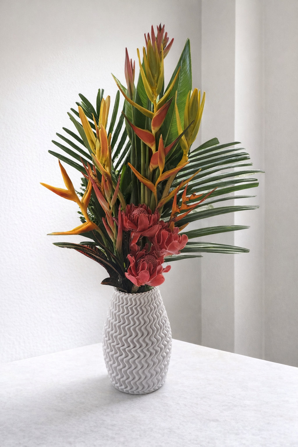 Tropical flower arrangement in a white textured vase on a light surface with a neutral background